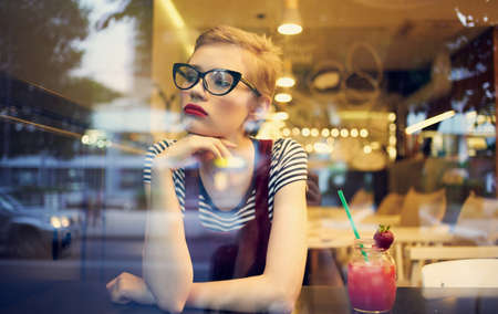fashionable woman in red sundress sits in a cafe and mirror glass reflection of cars on the streetの写真素材