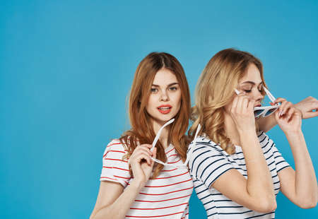 two mature women in trendy clothes striped t-shirts cropped blue background chatting