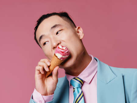 Asian man in a suit eating ice cream in a cone on a pink background business financeの写真素材
