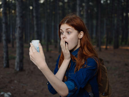 A woman travels in a pine forest with a mobile phone in her handの写真素材