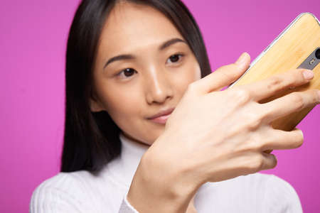 woman asian appearance phone in hands close-up technology gadget pink background