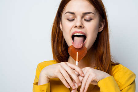emotional woman holding heart shaped lollipop yellow shirt isolated background
