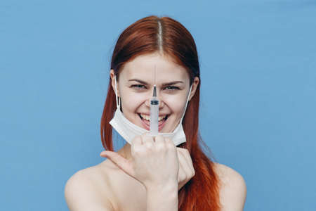 emotional woman with syringe in hand and medical mask injection vaccine blue backgroundの写真素材