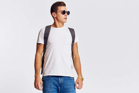 man in sunglasses with a backpack on his back and in a white t-shirt on a light background cropped...