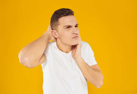 A man in a white T-shirt touches his face with his hand on a yellow background of emotionの写真素材