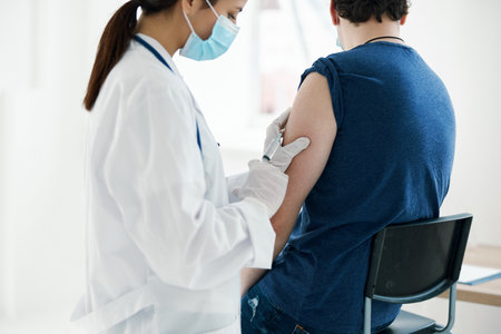 woman doctor in a medical mask injecting a man in a blue t-shirt covid vaccinationの写真素材