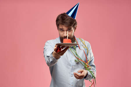 Man with cake in a plate and in a blue shirt on a pink background birthday holidays cropped view