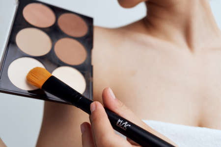 Pretty woman with naked shoulders applying makeup on face lifestyleの写真素材