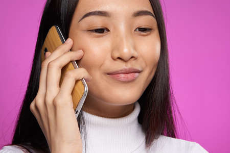 smiling asian woman talking on the phone technology pink backgroundの写真素材