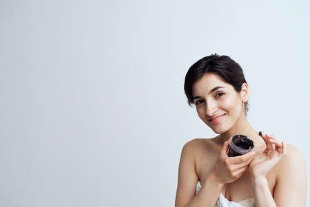 Pretty woman in white towel naked shoulders black cream in hands skin care spa procedureの写真素材