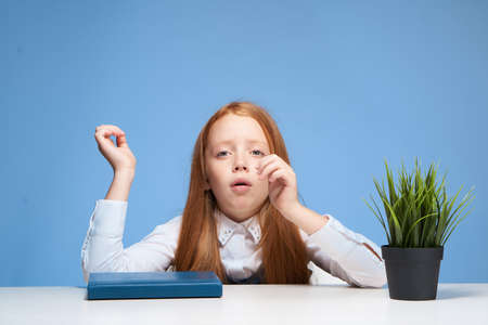 red-haired girl sitting at the school table book in hands educationの写真素材