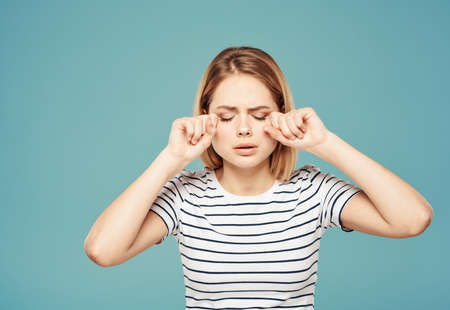 Cute blonde woman crying on a blue background and touching her face with her handsの写真素材
