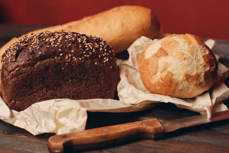 loaf of rye bread and flour products on paper packaging knife on a wooden table and red backgroundの写真素材