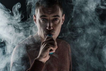 a man smokes a vape on a black background white smoke steam portrait close-up