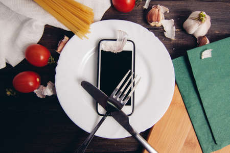 mobile phone plate knife with fork diet food pasta cherry tomatoesの写真素材