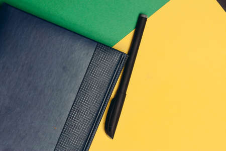 blue notebook and multicolored pens on yellow green background work office