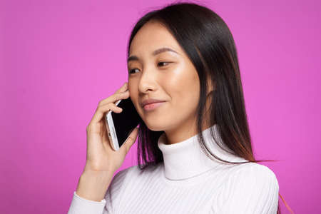 pretty brunette talking on the phone white sweater cropped view pink background