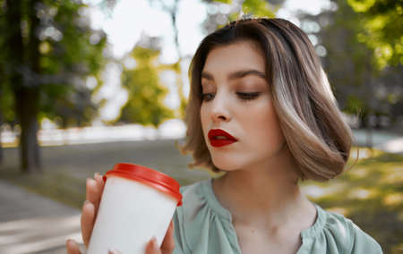 woman with a cup of drink in hand walks in the park in nature