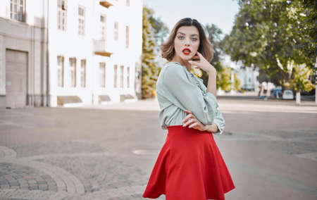 woman with bright makeup in a shirt and in a red skirt are walking on the street in summer near the buildingの写真素材