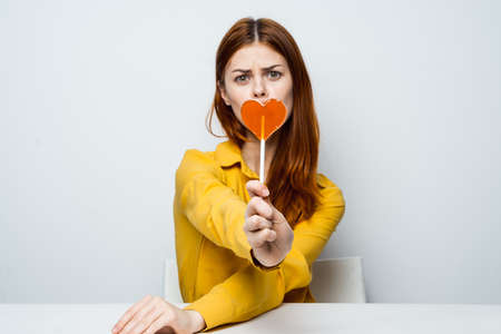 pretty woman in a yellow shirt with a heart-shaped lollipop in her handsの写真素材