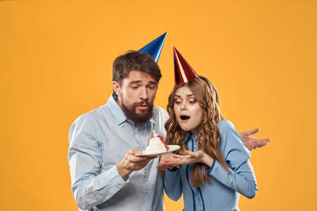 Birthday party man and woman in a cap with a cake on a yellow background cropped viewの写真素材