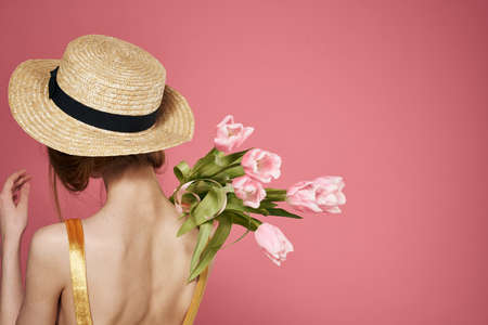 Woman in a hat bouquet of flowers in a dress rear view pink background