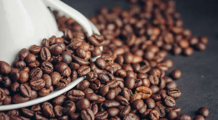 white cup and saucer and large coffee beans on a dark background macro photography