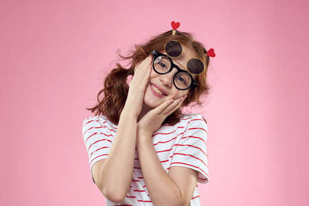 little girl in fashionable glasses and clothespins on her hair emotions pink background heartsの写真素材