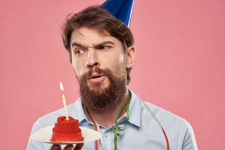 Man with a cake with a candle and a birthday cap on a pink backgroundの写真素材