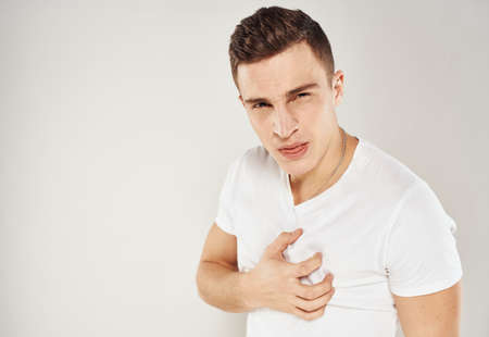 Guy in a white T-shirt sadness emotions model light background gesticulate with his handsの写真素材