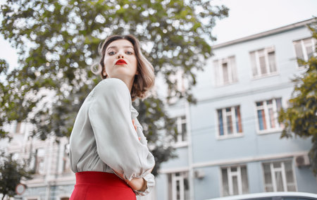 woman with red lips in a fashionable shirt near the building and green trees spring natureの写真素材