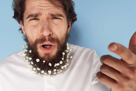 Emotional man in a white T-shirt flowers in a beard close-up blue backgroundの写真素材