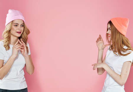 two cute girlfriends wearing t-shirts fashionable hats communication lifestyle pink backgroundの写真素材