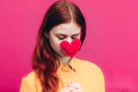 happy woman with red heart on stick on pink background and yellow shirtの写真素材
