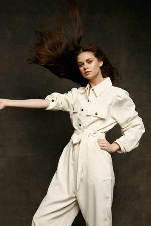 a pretty brunette in a light jumpsuit gestures with her hands on a dark backgroundの写真素材
