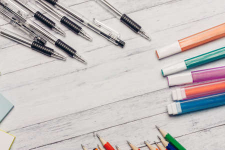 markers pencils pens on a wooden table and colored paper office stationeryの写真素材