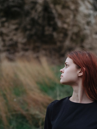 Portrait of a woman in a black dress outdoors on a meadow in the mountains