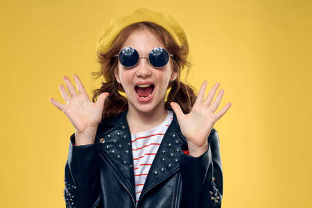 Cheerful little girl in sunglasses and hat lifestyle studio yellow background fashionの写真素材