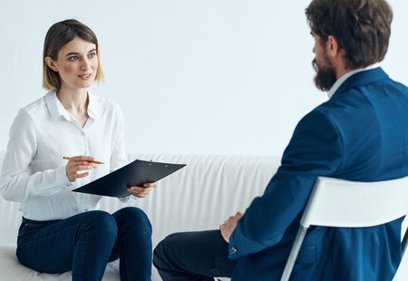 A woman psychologist with documents sits on the couch and a man on a chair in a suitの写真素材