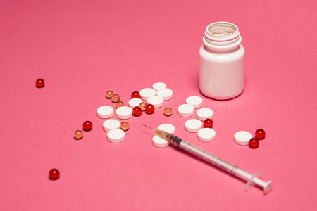 A jar of pills and a syringe with a needle on a pink background side viewの写真素材