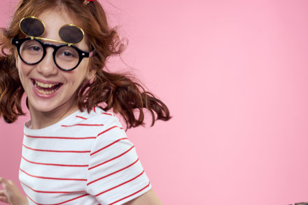 little girl in fashionable glasses and clothespins on her hair emotions pink background heartsの写真素材