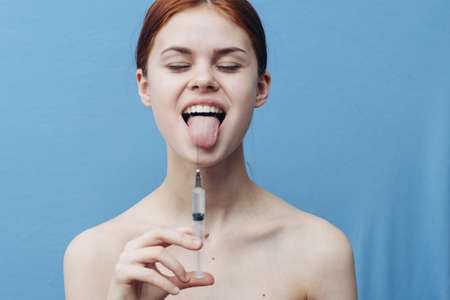 emotional red-haired woman on blue background holding syringe in hand cropped viewの写真素材