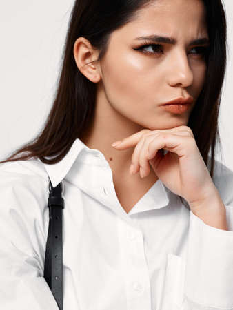brunette woman in light shirt looks to the side and holds her hand near her face