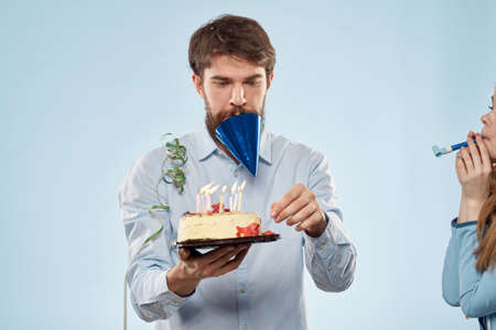 Man with a plate of cake and a festive candle blue background cap corporate partyの写真素材