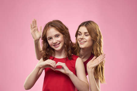 Cheerful mom and daughter wearing red dresses are standing next to joy family on pink backgroundの写真素材