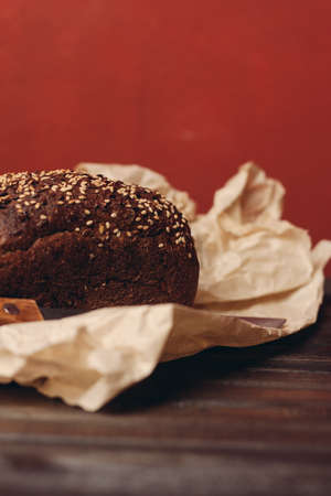 rye bread on paper packaging on a red background and a wooden table with a sharp knifeの写真素材