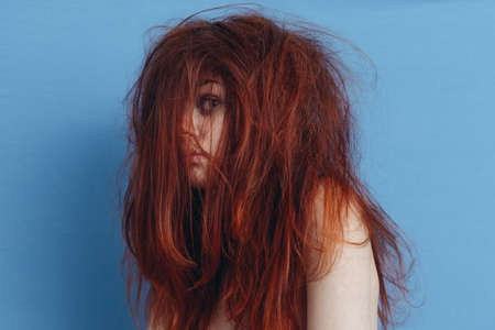 red-haired woman touching her head with hands emotions tousled hair blue backgroundの写真素材