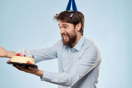 Man with a plate of cake and a festive candle blue background cap corporate partyの写真素材