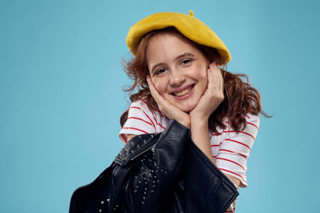 Fashionable girl in a yellow beret and leather jacket striped T-shirt blue backgroundの写真素材