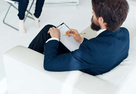A business man in a suit sits on a white sofa In a bright room, side viewの写真素材